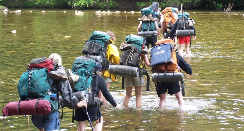 A group of students wearing backpacks make their way through ankle-deep water.